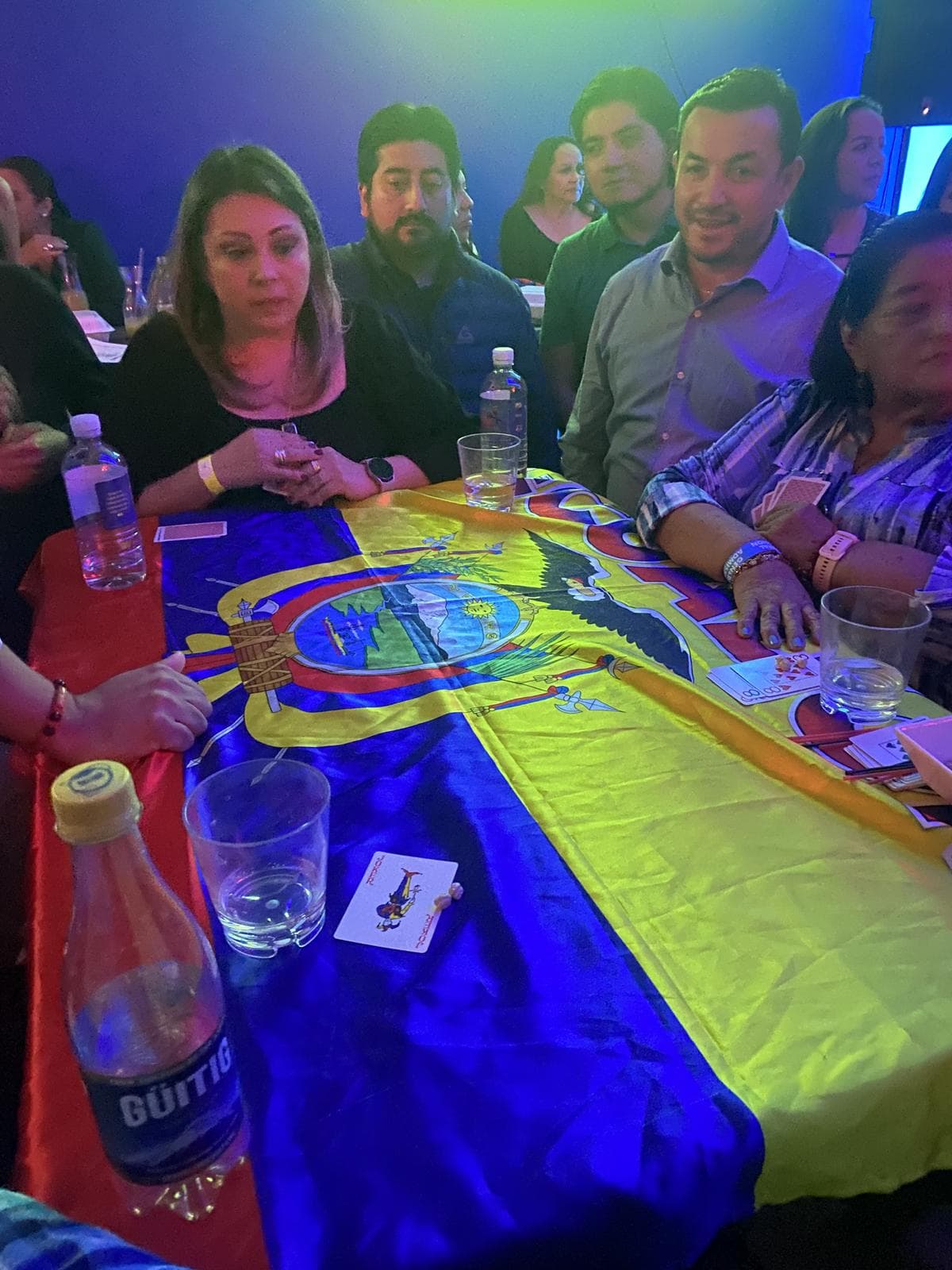 Jugadores alrededor de una mesa cubierta con la bandera del Ecuador, con las cartas repartidas